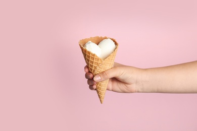 Woman holding delicious ice cream in wafer cone on pink background, closeup