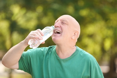Photo of Elderly man drinking water outdoors on sunny day