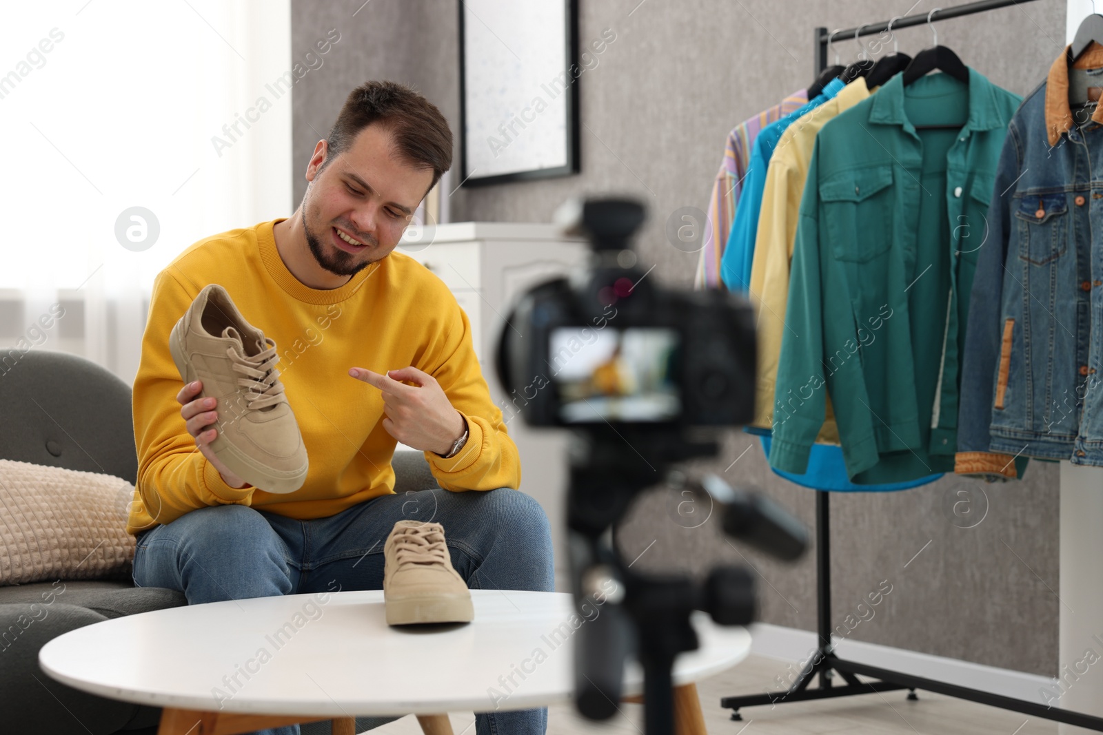 Photo of Smiling fashion blogger showing shoes while recording video at home