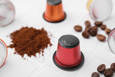 Coffee capsules, powder and beans on white tiled table, closeup