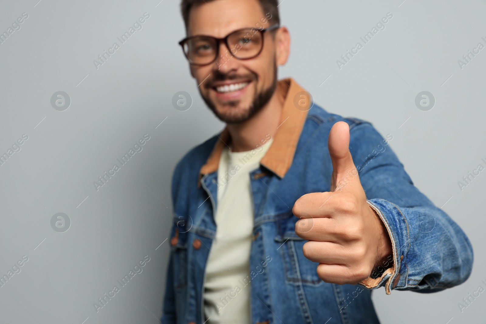 Photo of Man showing thumb up against grey background, focus on hand. Space for text