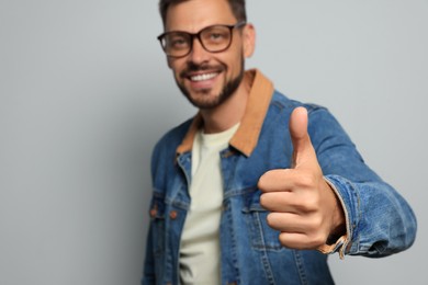 Man showing thumb up against grey background, focus on hand. Space for text