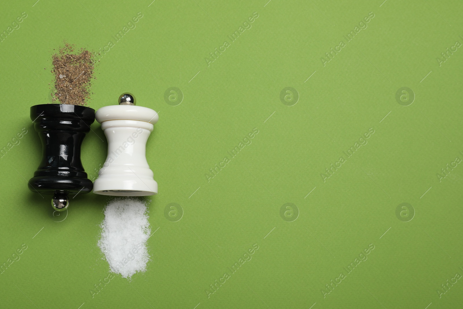 Photo of Salt and pepper shakers on green table, flat lay. Space for text