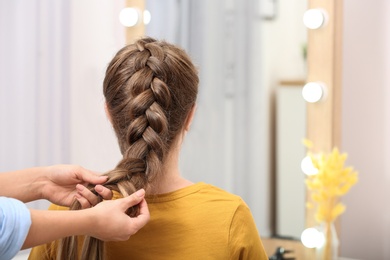 Photo of Professional coiffeuse braiding client's hair in salon