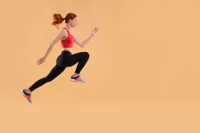 Photo of Young woman in sportswear jumping on beige background, space for text