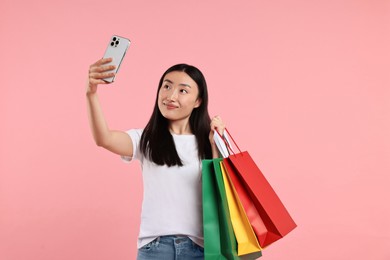 Smiling woman with shopping bags taking selfie on pink background. Space for text
