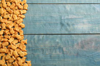 Photo of Delicious goldfish crackers on blue wooden table, flat lay. Space for text