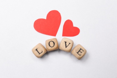 Photo of Mini cubes with letters forming word Love near red paper hearts on white background, flat lay