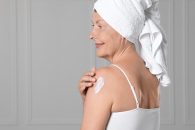 Happy woman applying body cream onto shoulder near white wall. Space for text