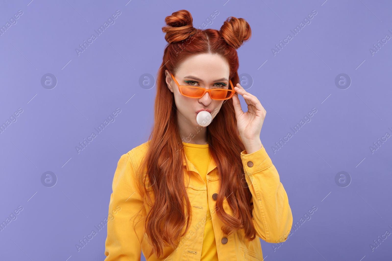 Photo of Portrait of beautiful woman in sunglasses blowing bubble gum on violet background
