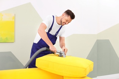 Dry cleaning worker removing dirt from sofa cushion indoors