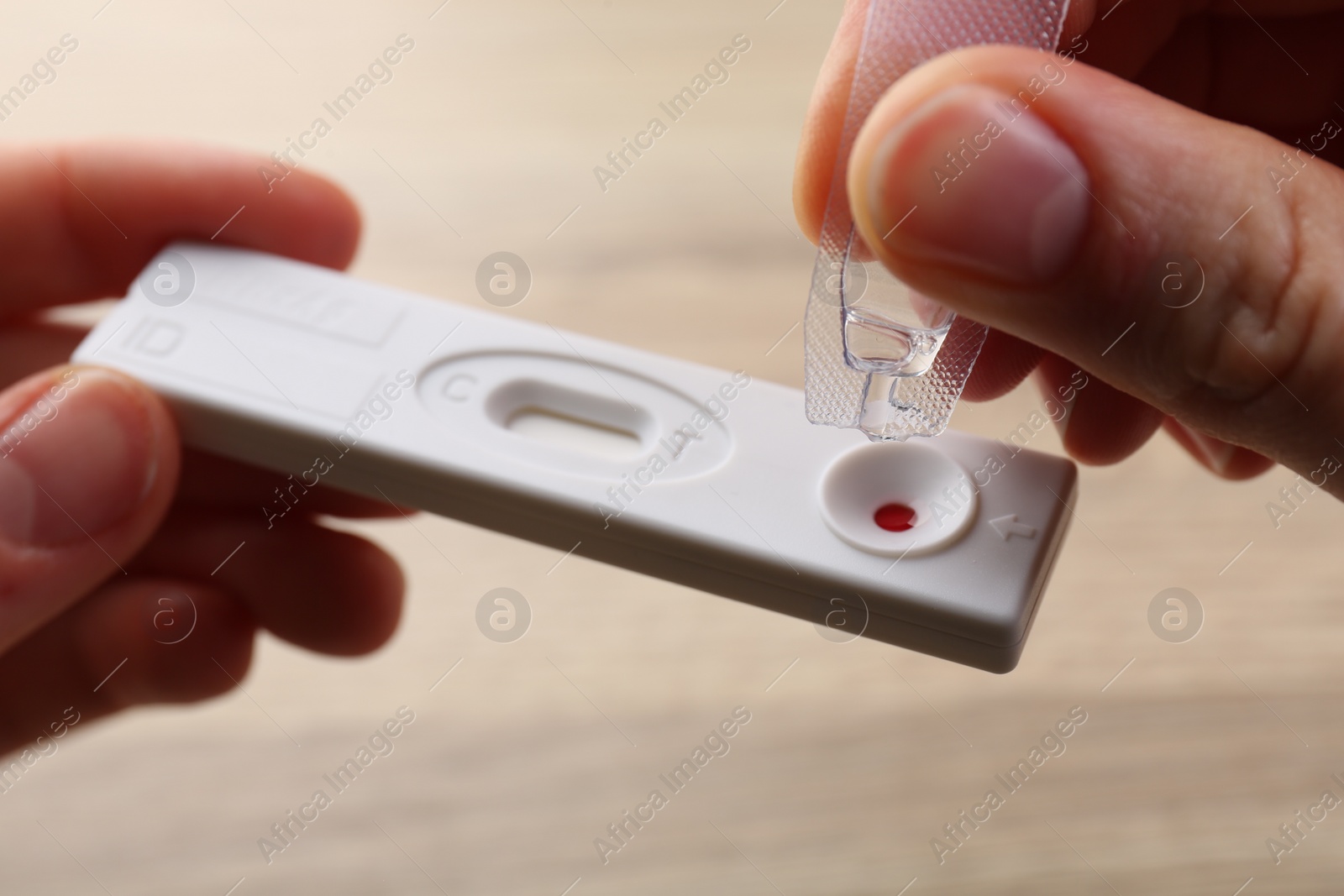 Photo of Woman dropping buffer solution onto disposable express test cassette on blurred background, closeup