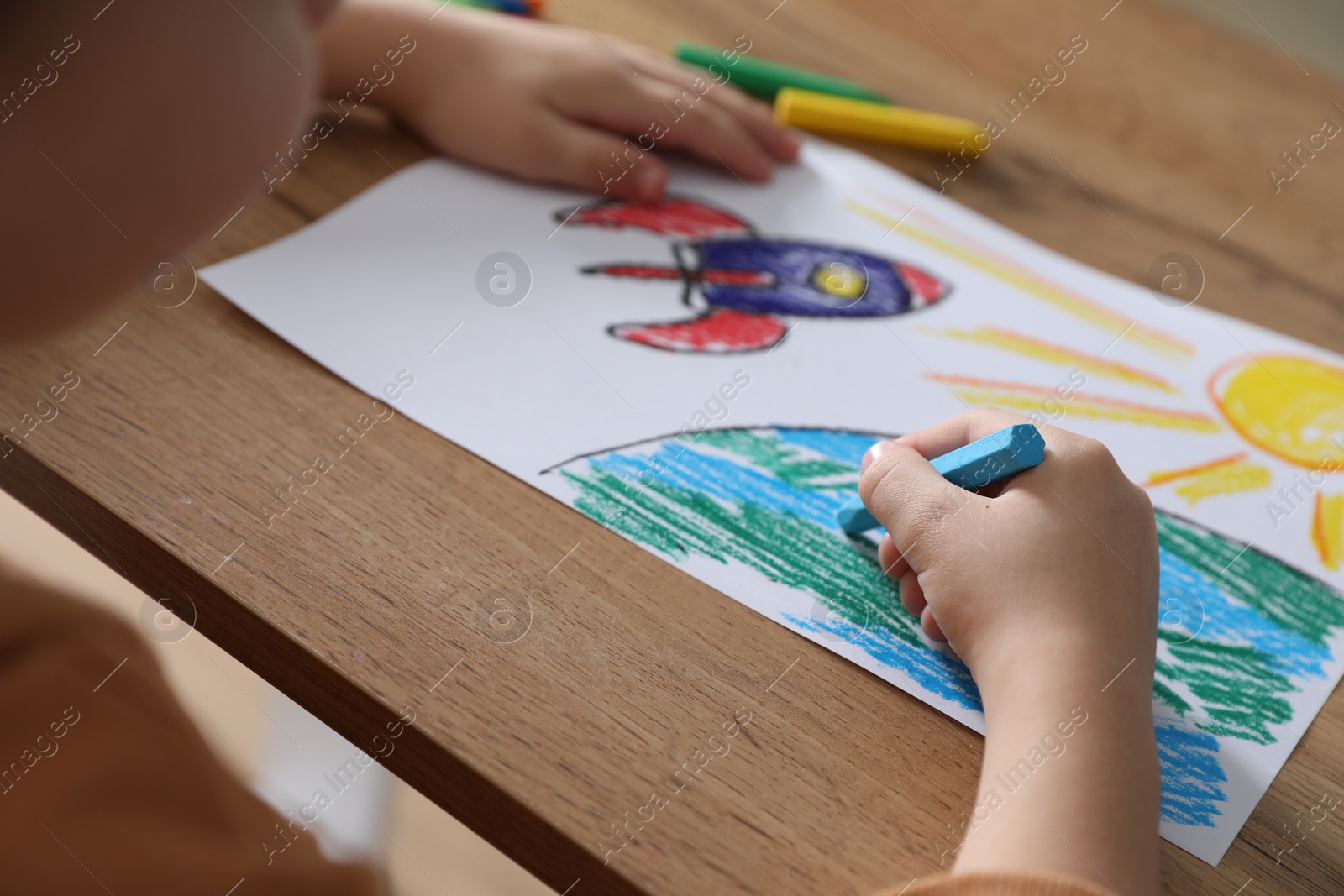 Photo of Little girl drawing picture with soft pastel at wooden table, closeup. Child`s art