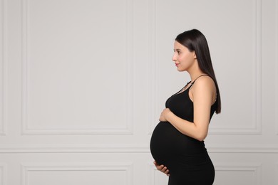 Photo of Beautiful pregnant woman in black dress near light grey wall, space for text