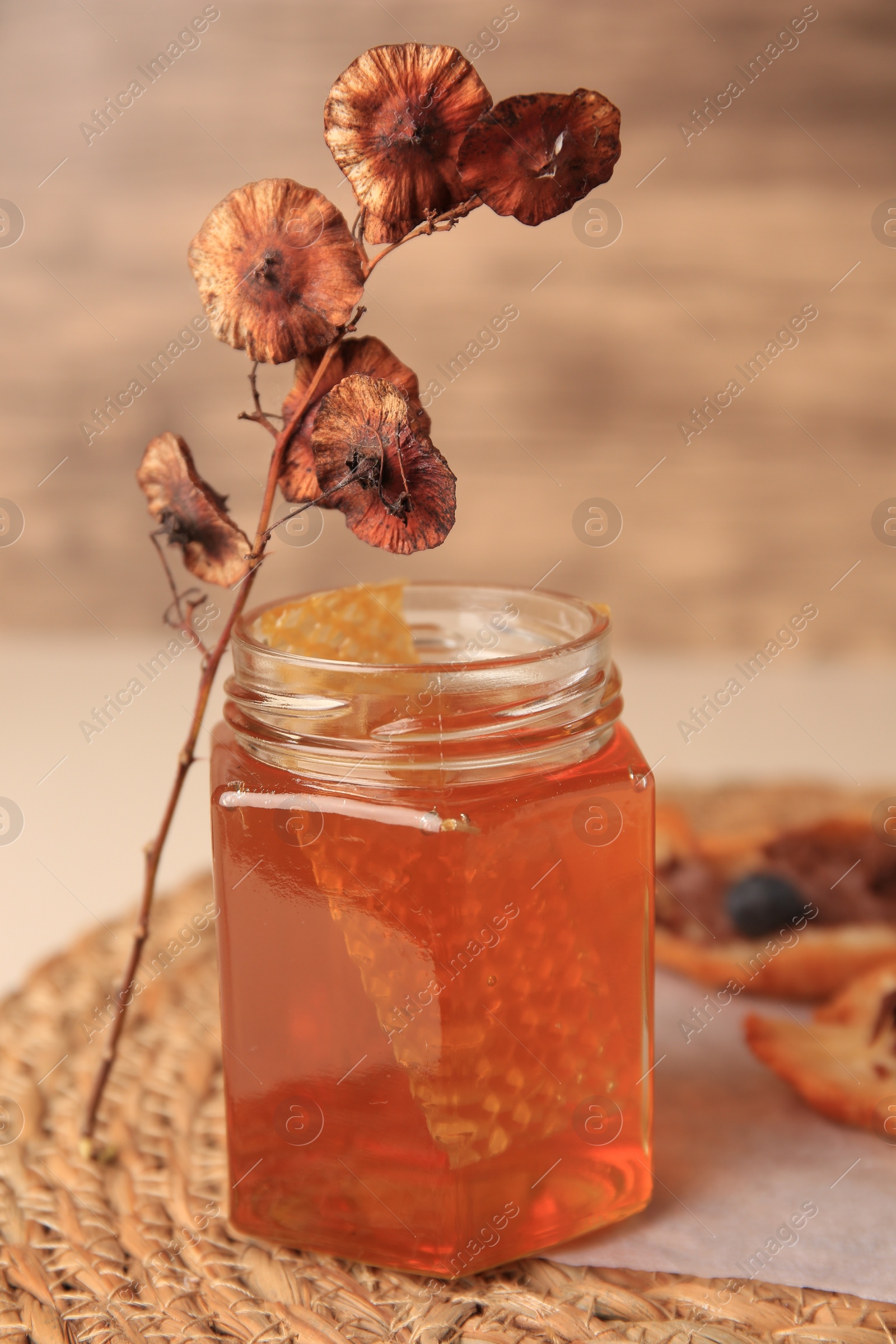 Photo of Glass jar with honey and combs on wicker mat, closeup