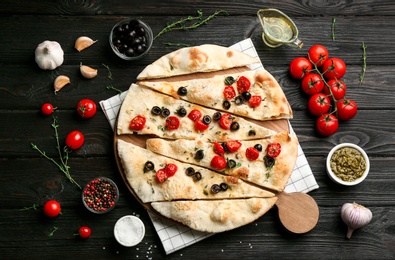 Delicious focaccia bread with olives and tomatoes on black wooden table, flat lay