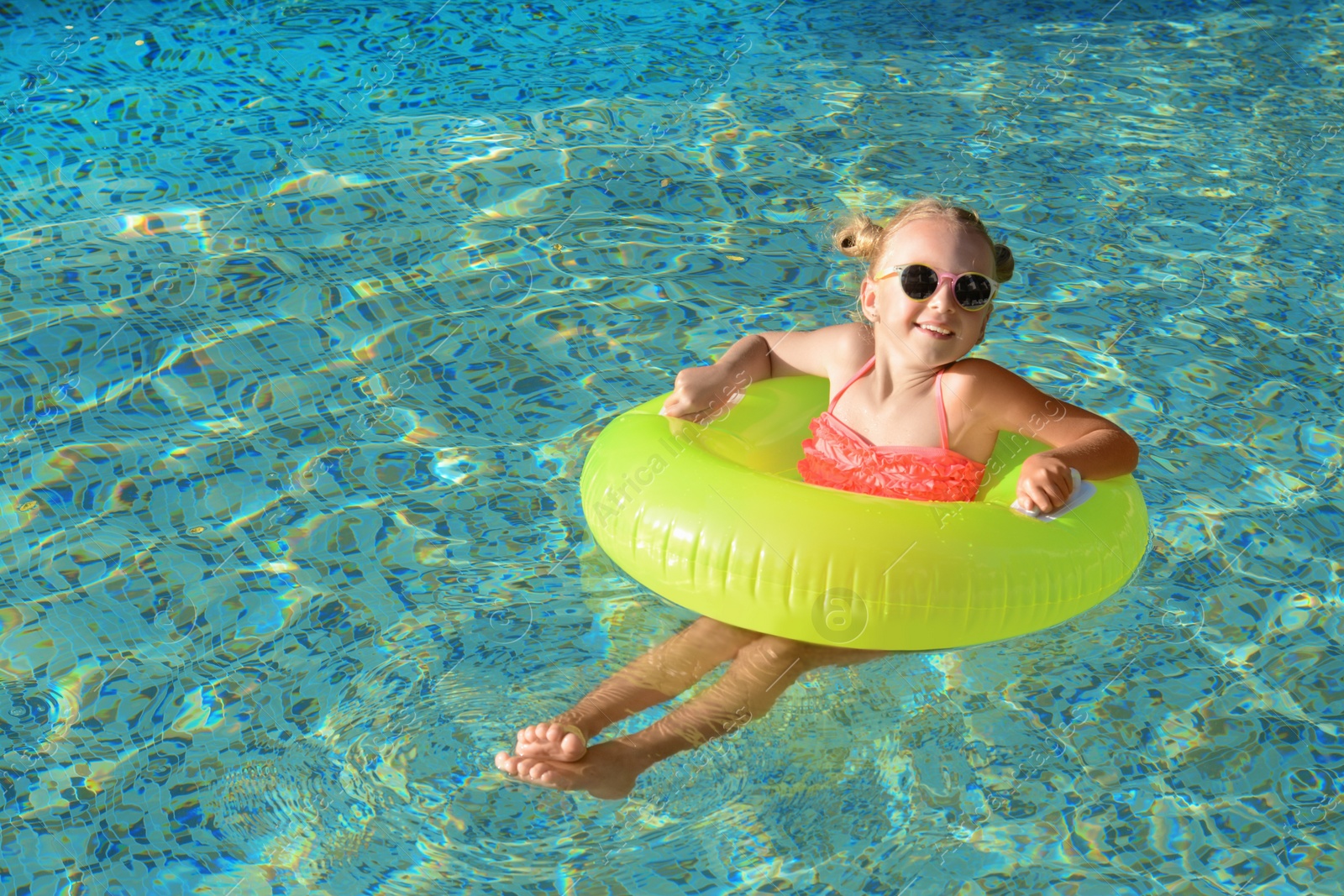 Photo of Happy little girl with inflatable ring in outdoor swimming pool on sunny day, space for text