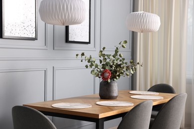 Soft chairs, table and vase with plants in stylish dining room