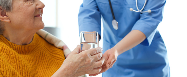 Image of Care worker giving water to elderly woman in geriatric hospice, closeup. Banner design