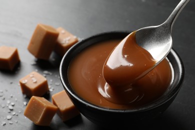 Photo of Taking yummy salted caramel with spoon from bowl on table, closeup