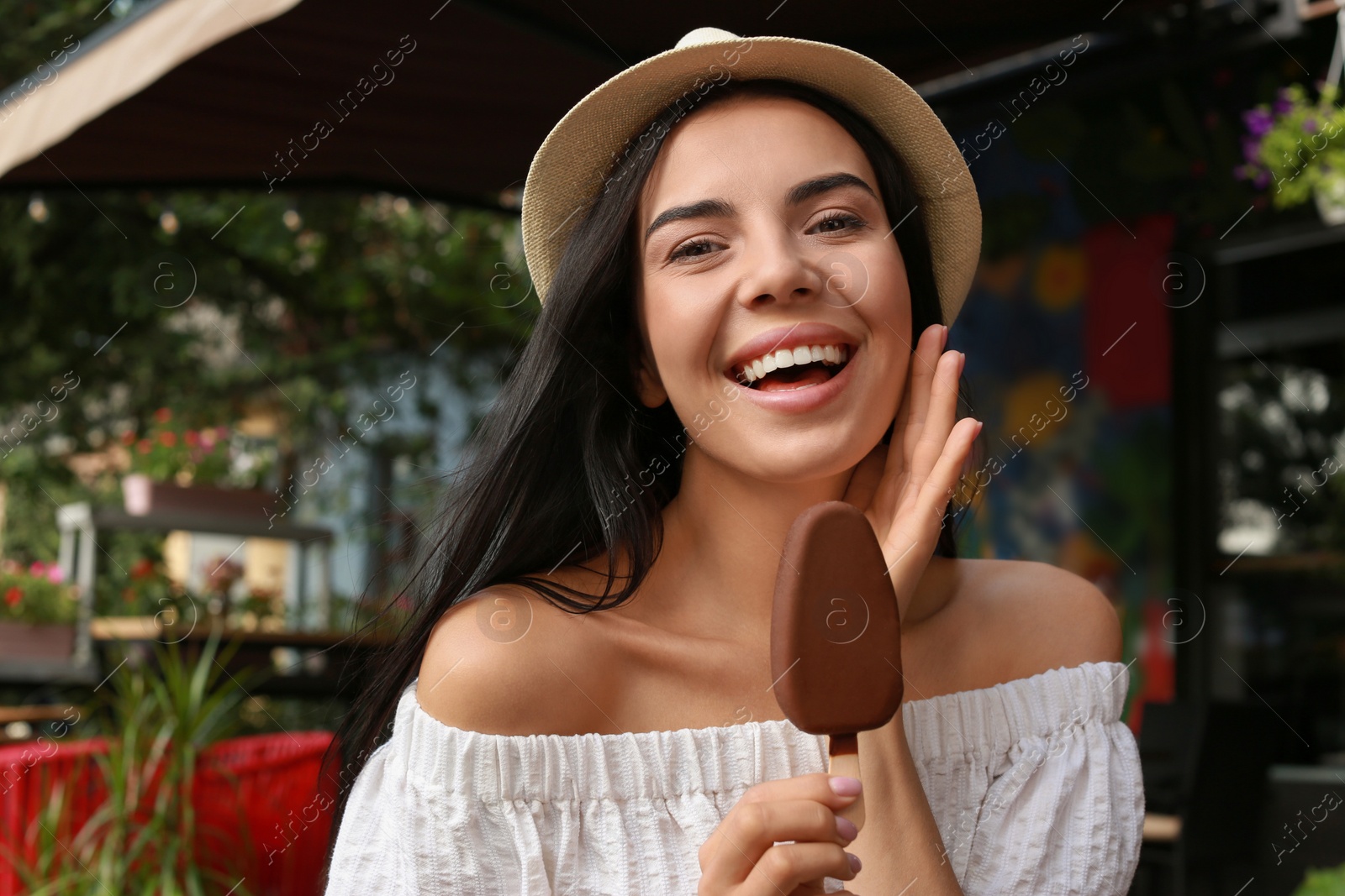 Photo of Beautiful young woman holding ice cream glazed in chocolate on city street