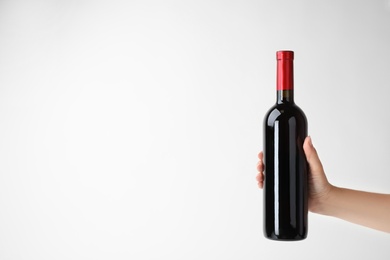 Photo of Woman holding bottle of expensive red wine on light background