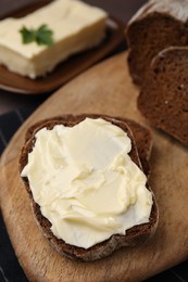 Photo of Slices of tasty bread with butter on wooden board, closeup