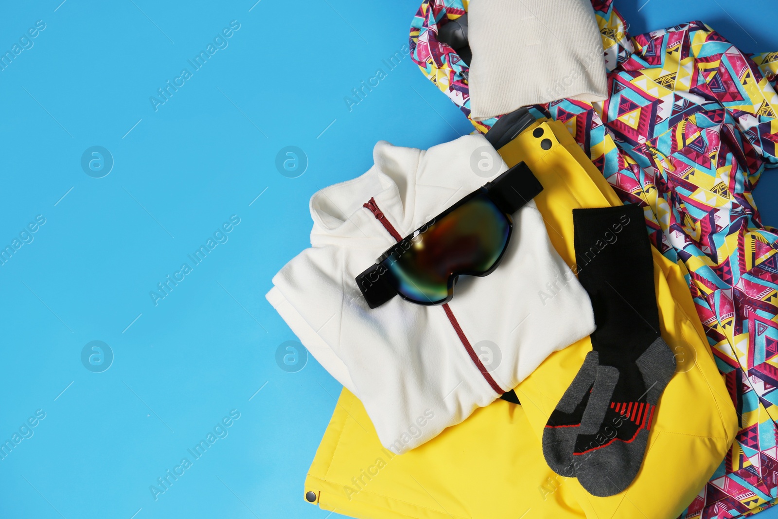 Photo of Stylish winter sport clothes on light blue background, flat lay. Space for text