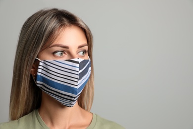Young woman in protective face mask on light grey background. Space for text
