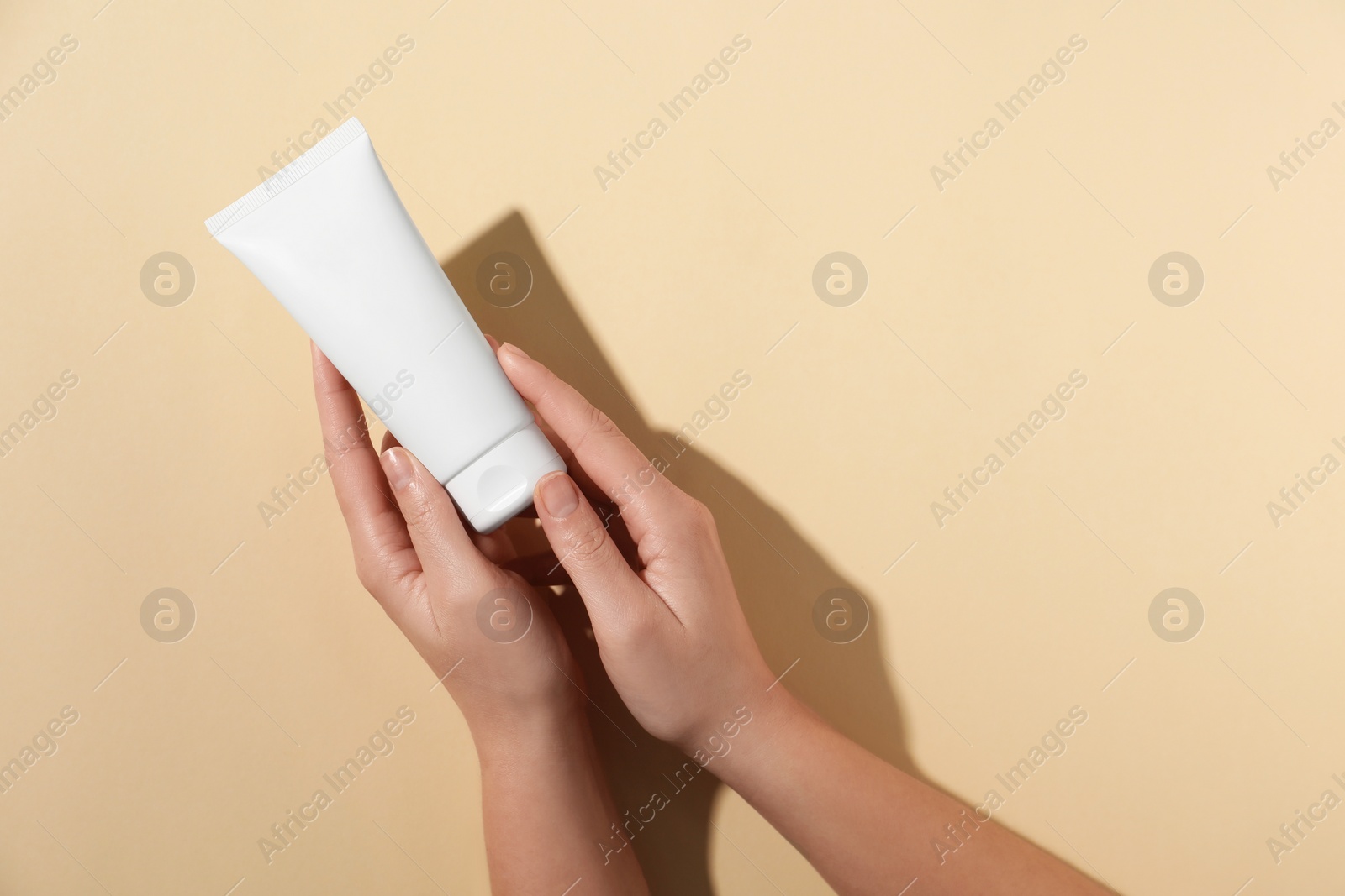 Photo of Woman with tube of hand cream on beige background, top view. Space for text