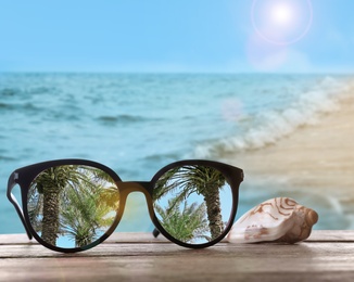 Palms mirroring in sunglasses on wooden desk with seashell at sandy beach