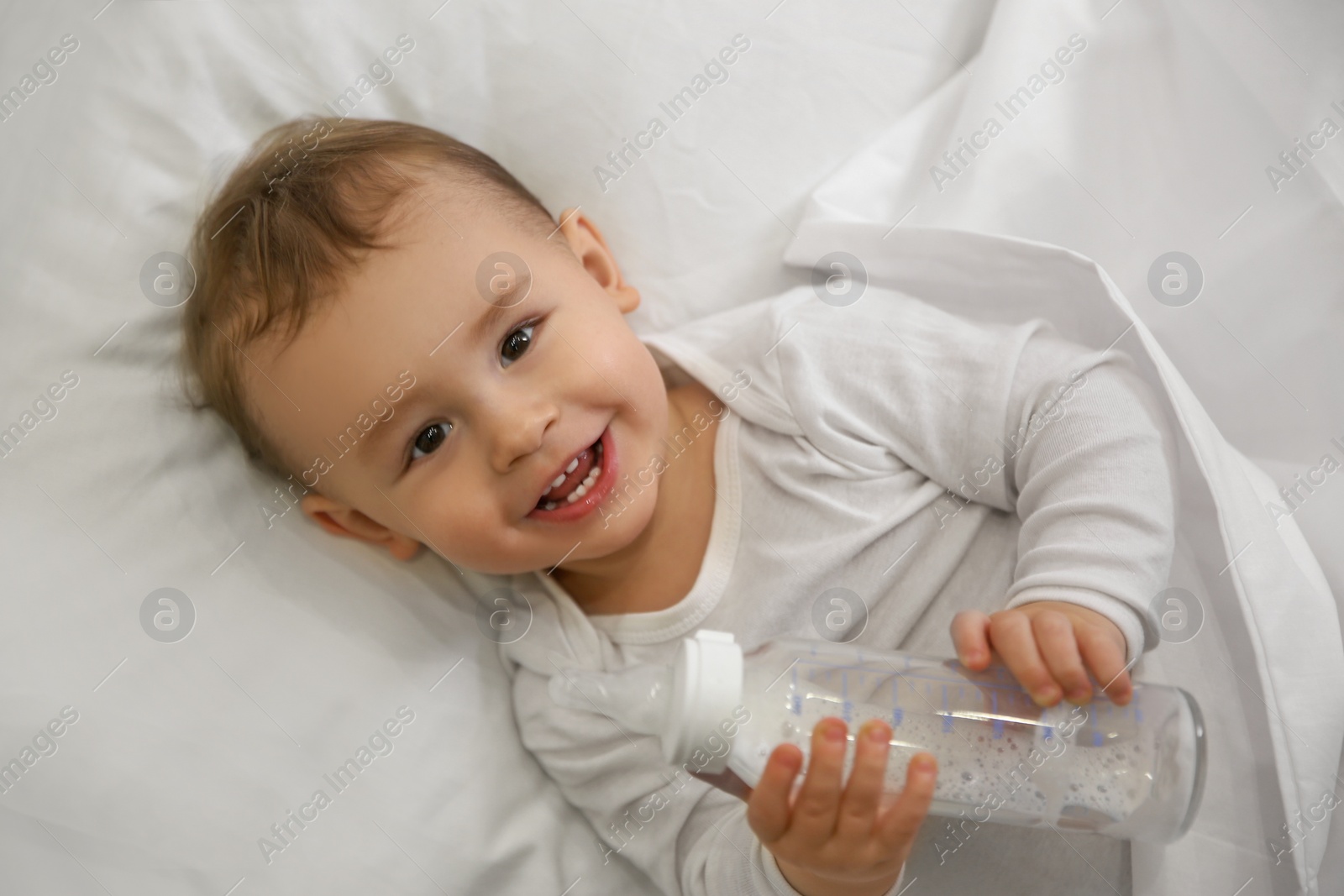 Photo of Cute little baby with bottle lying in comfortable crib, top view. Bedtime