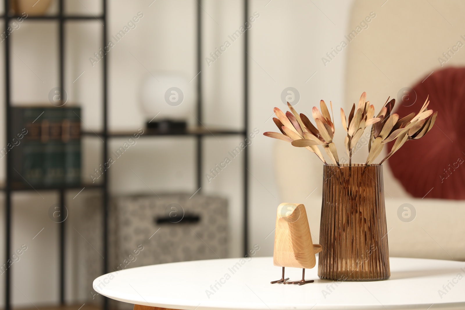 Photo of Vase with beautiful dried leucadendron plants and wooden bird on white table in living room, space for text