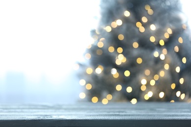 Photo of Blurred view of beautiful Christmas tree with yellow lights near window indoors, focus on wooden table. Space for text