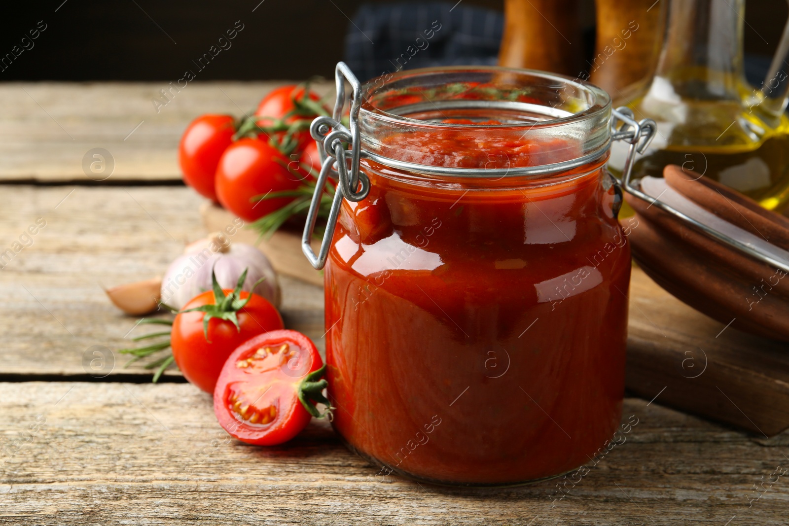 Photo of Homemade tomato sauce in jar and fresh ingredients on wooden table, closeup