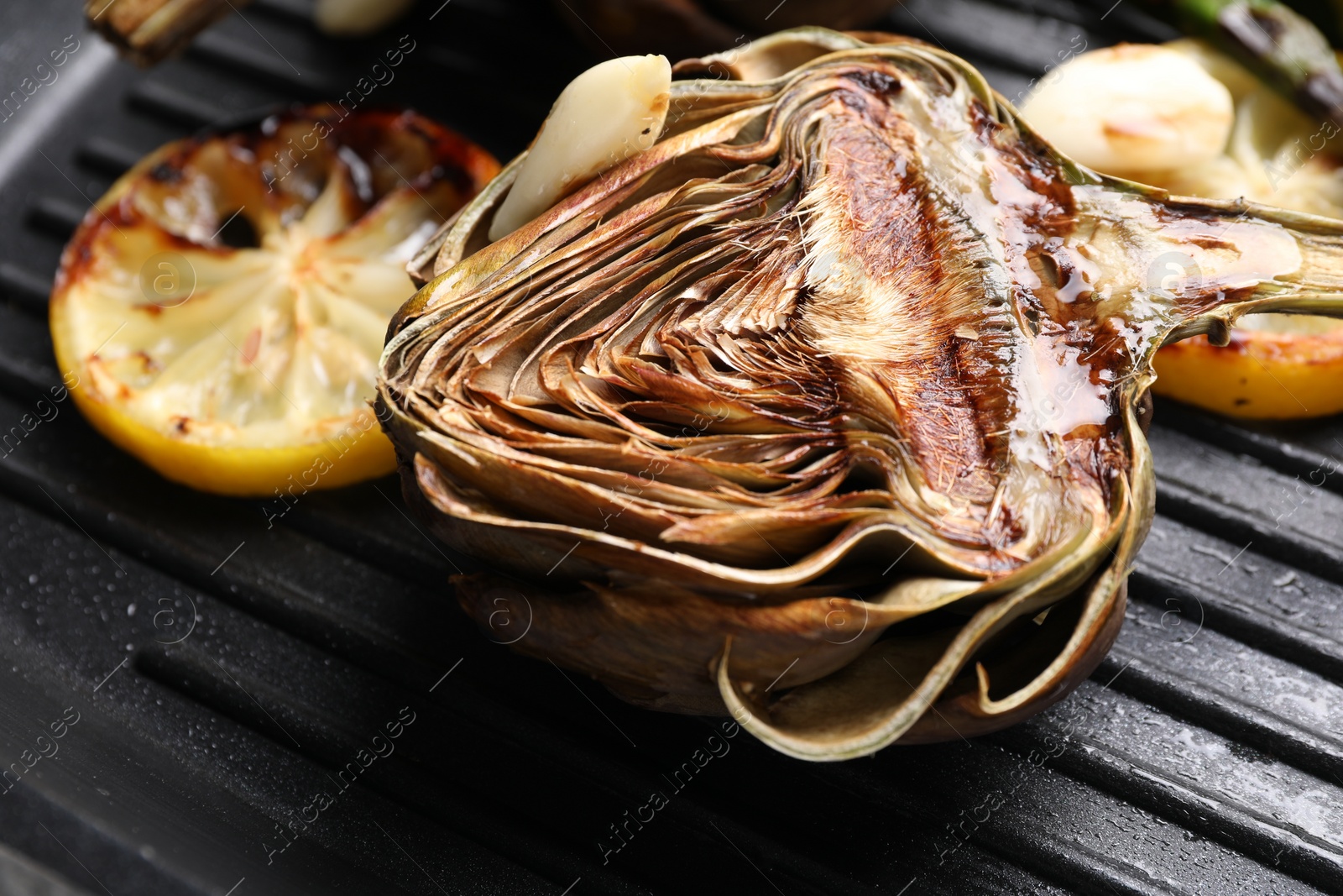 Photo of Tasty grilled artichoke and slices of lemon in pan, closeup
