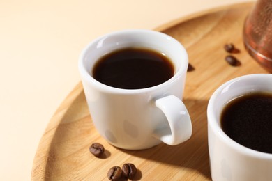 Photo of Delicious coffee in cups and beans on beige table, closeup