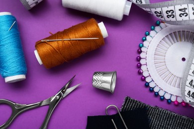 Flat lay composition with thimble and different sewing tools on purple background