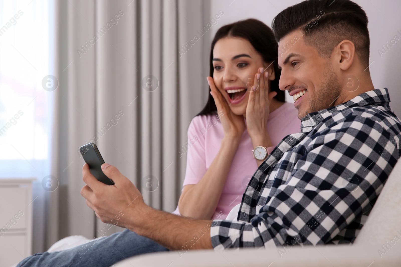 Photo of Emotional couple participating in online auction using smartphone at home