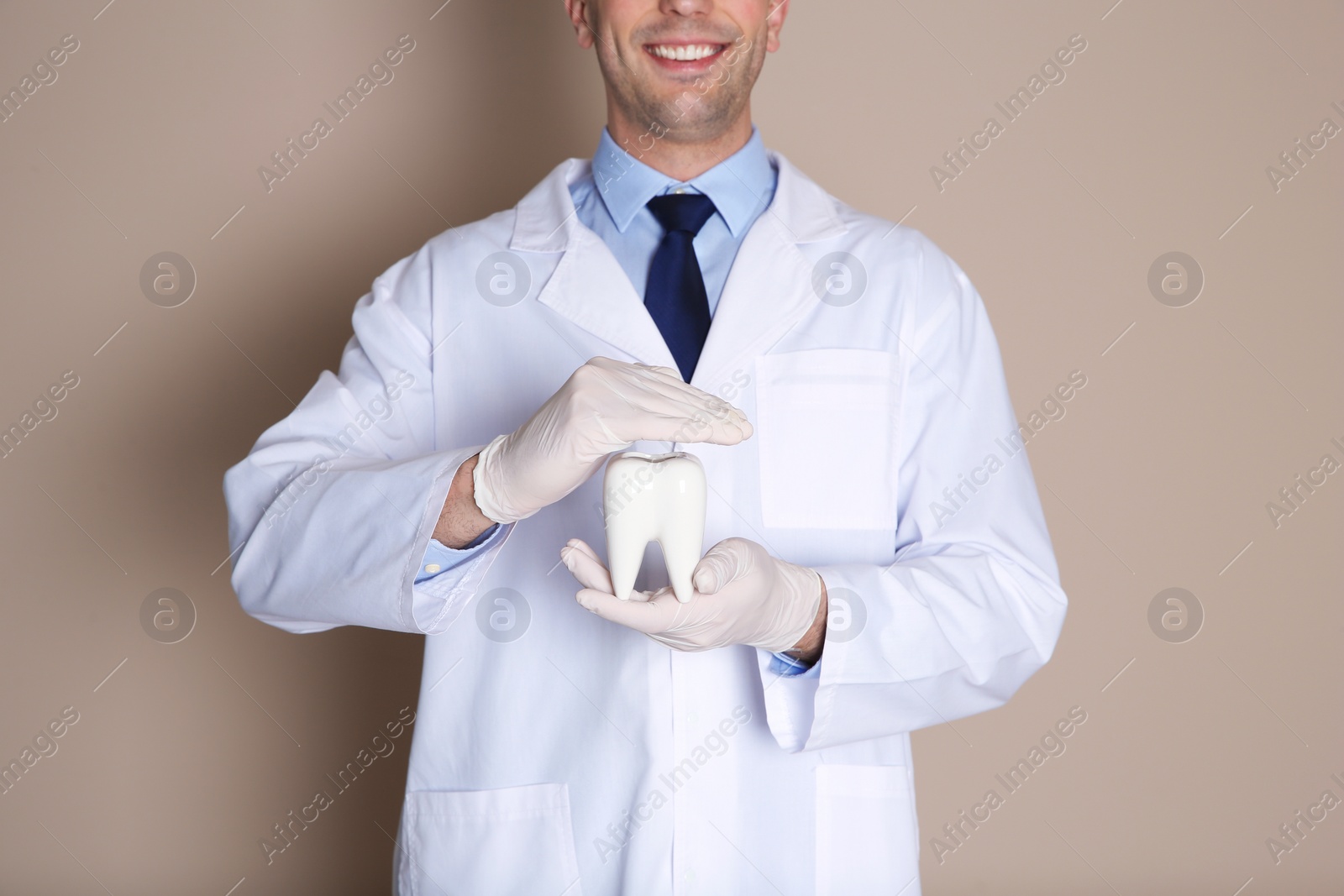 Photo of Male dentist holding tooth model on color background, closeup