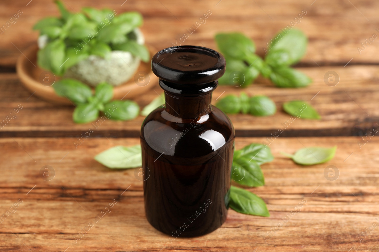 Photo of Glass bottle of basil essential oil and leaves on wooden table