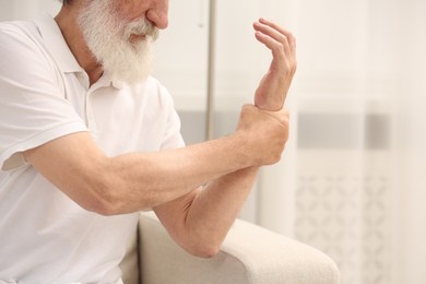 Photo of Senior man suffering from pain in hand at home, closeup. Rheumatism symptom