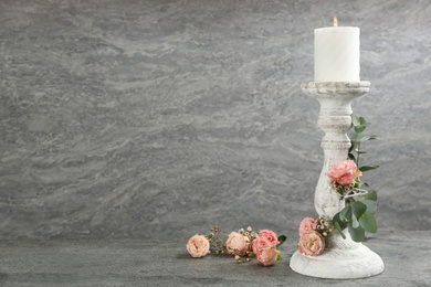 Photo of Vintage candlestick with burning candle, roses and eucalyptus on grey table. Space for text