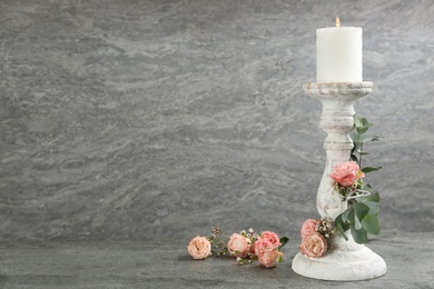 Vintage candlestick with burning candle, roses and eucalyptus on grey table. Space for text