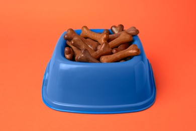 Blue bowl with bone shaped dog cookies on orange background, closeup