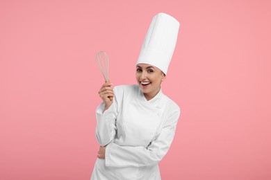 Photo of Happy professional confectioner in uniform holding whisk on pink background