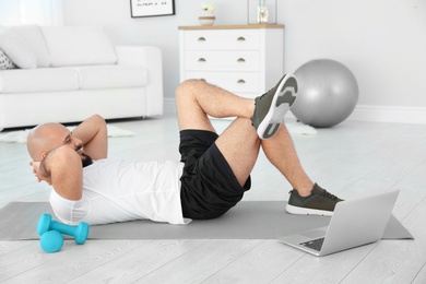 Photo of Overweight man doing exercise while watching tutorial on laptop at home