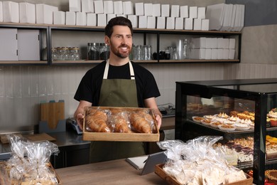 Photo of Happy seller with croissants at cashier desk in bakery shop