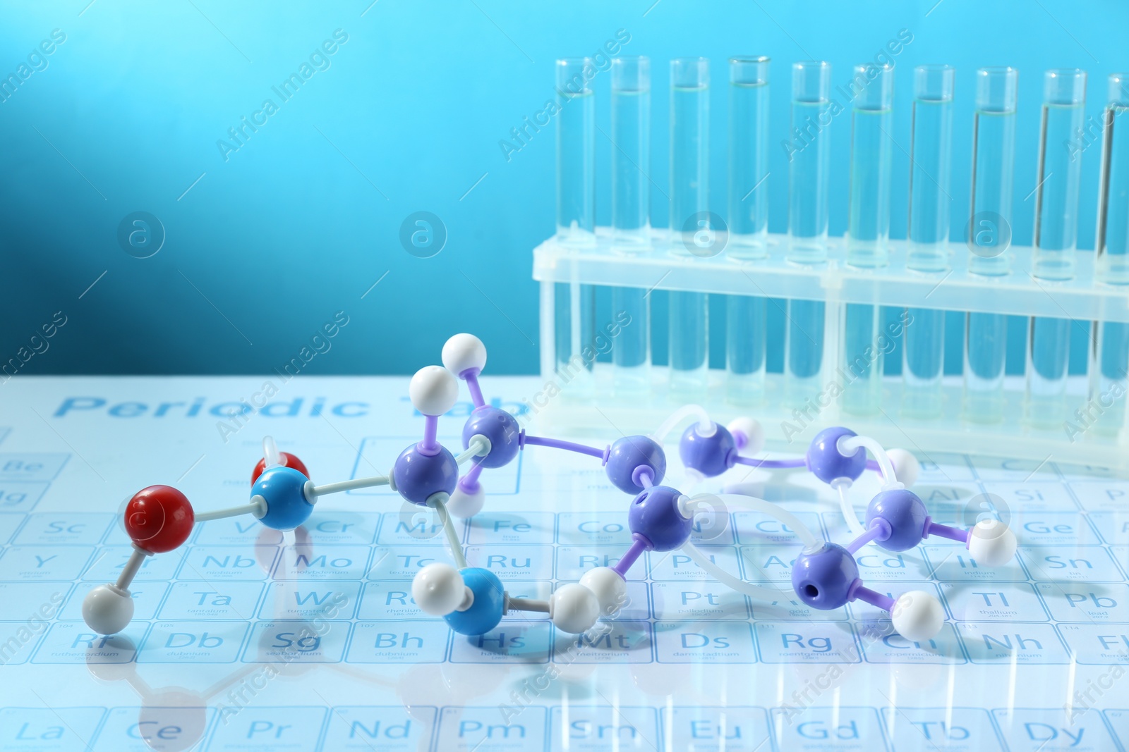 Photo of Molecular model and test tubes on periodic table against light blue background