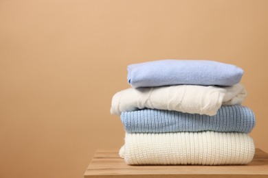 Photo of Stack of casual sweaters on wooden table against light brown background. Space for text